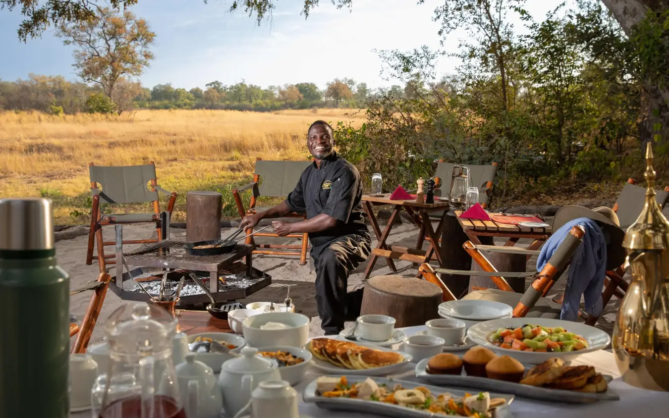 Outdoor dining setup with staff and meal service in savanna, Selinda Explorers Camp, Selinda Reserve, Botswana