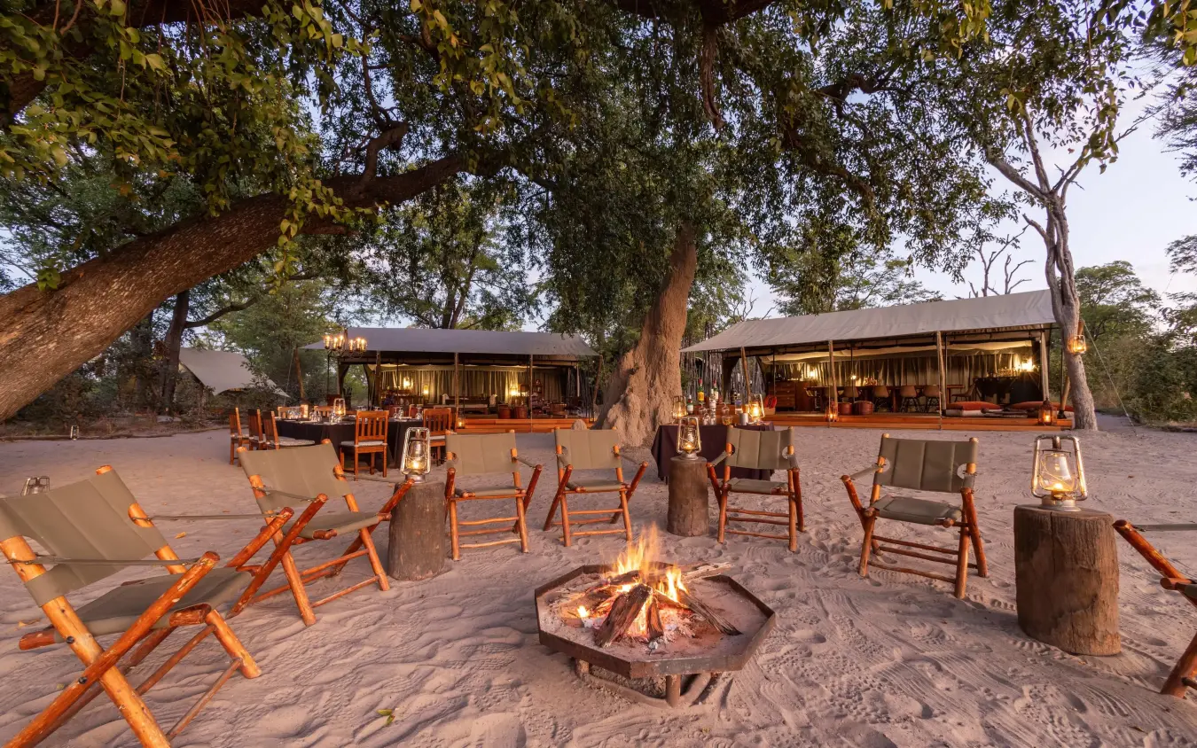 Safari camp gathering area with fire pit and seating at dusk, Selinda Explorers Camp, Selinda Reserve, Botswana