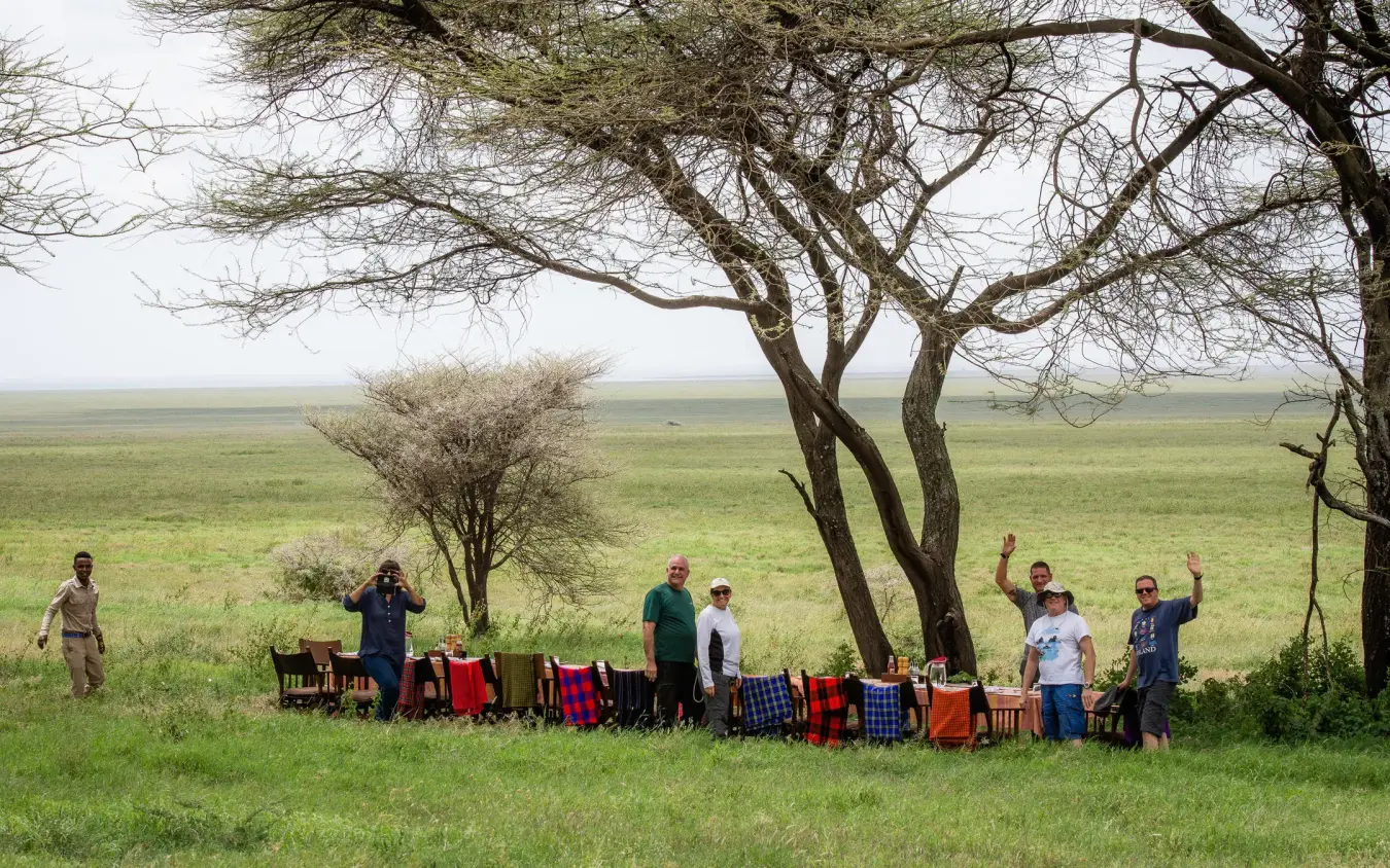 Group gathered under acacia tree in savanna landscape, Esirai Camp, Serengeti National Park, Tanzania
