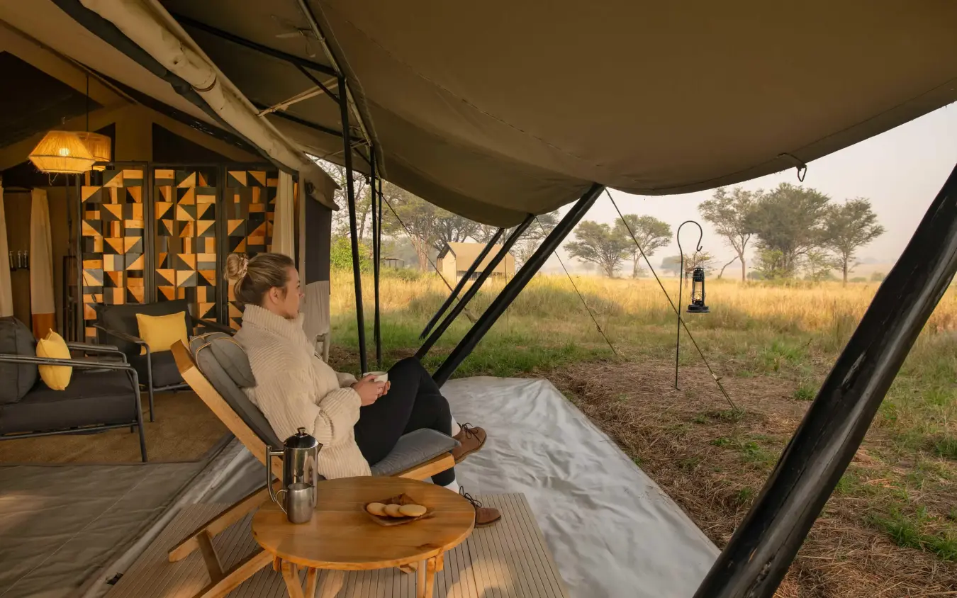 Guest relaxing on canvas deck overlooking savanna landscape, Ubuntu Migration Camp, Serengeti National Park, Tanzania