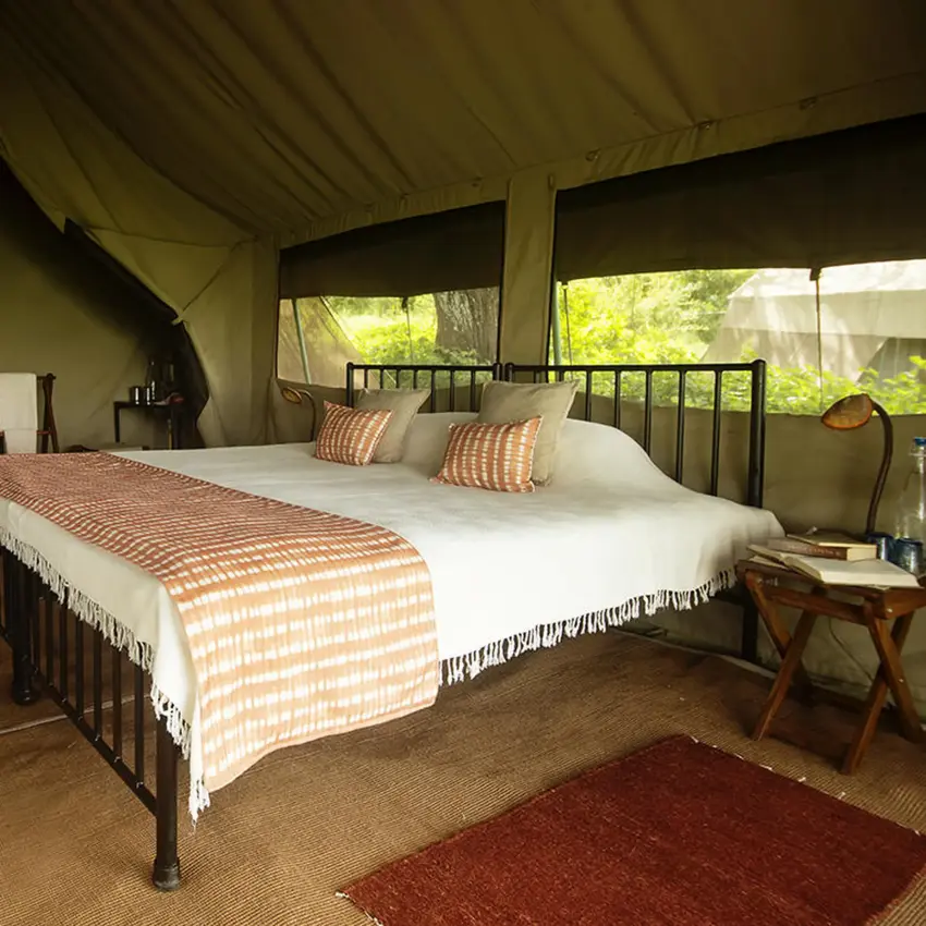 Canvas safari tent bedroom with white linens and striped accents, Esirai Camp, Serengeti National Park, Tanzania