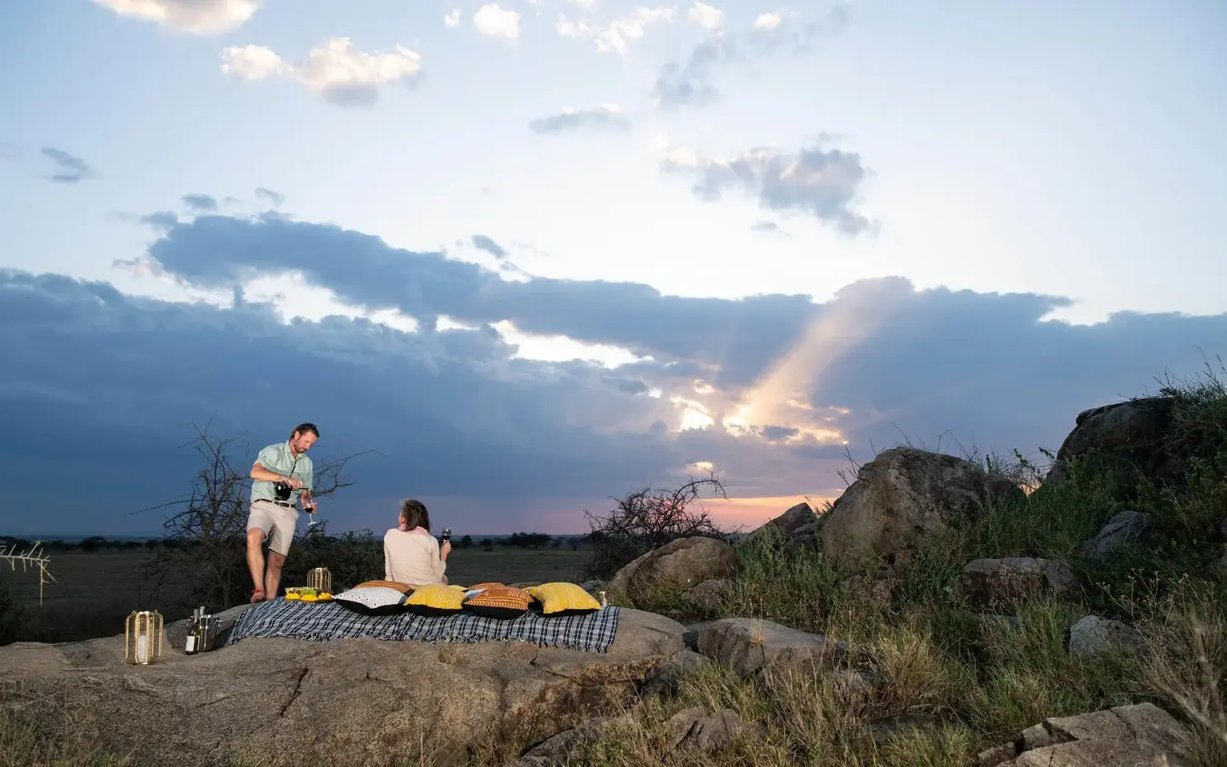 Couple dining outdoors at sunset on rocky outcrop, Serengeti Plains Camp, Serengeti National Park, Tanzania