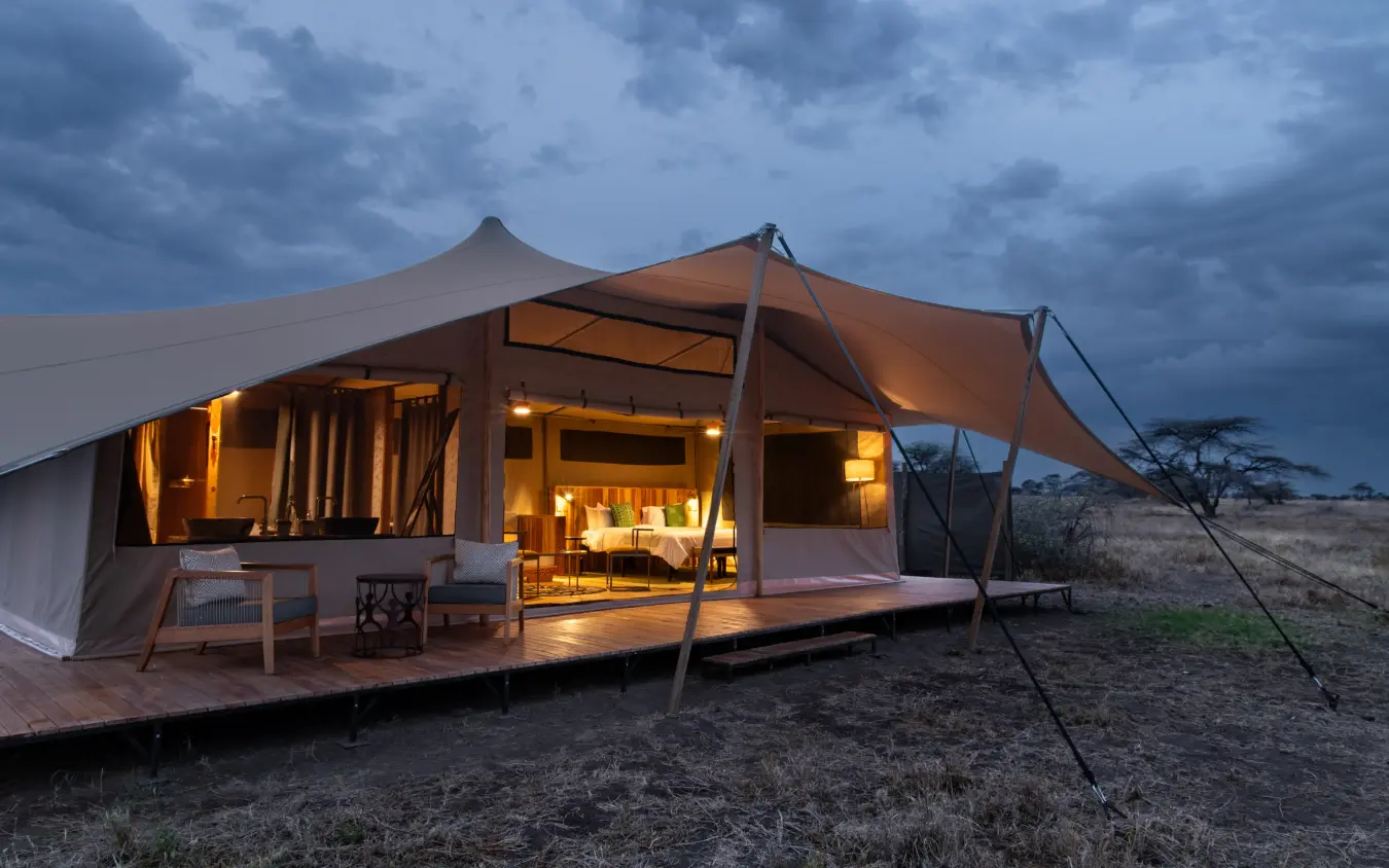 Illuminated safari tent with wooden deck at dusk, Serengeti Plains Camp, Serengeti National Park, Tanzania