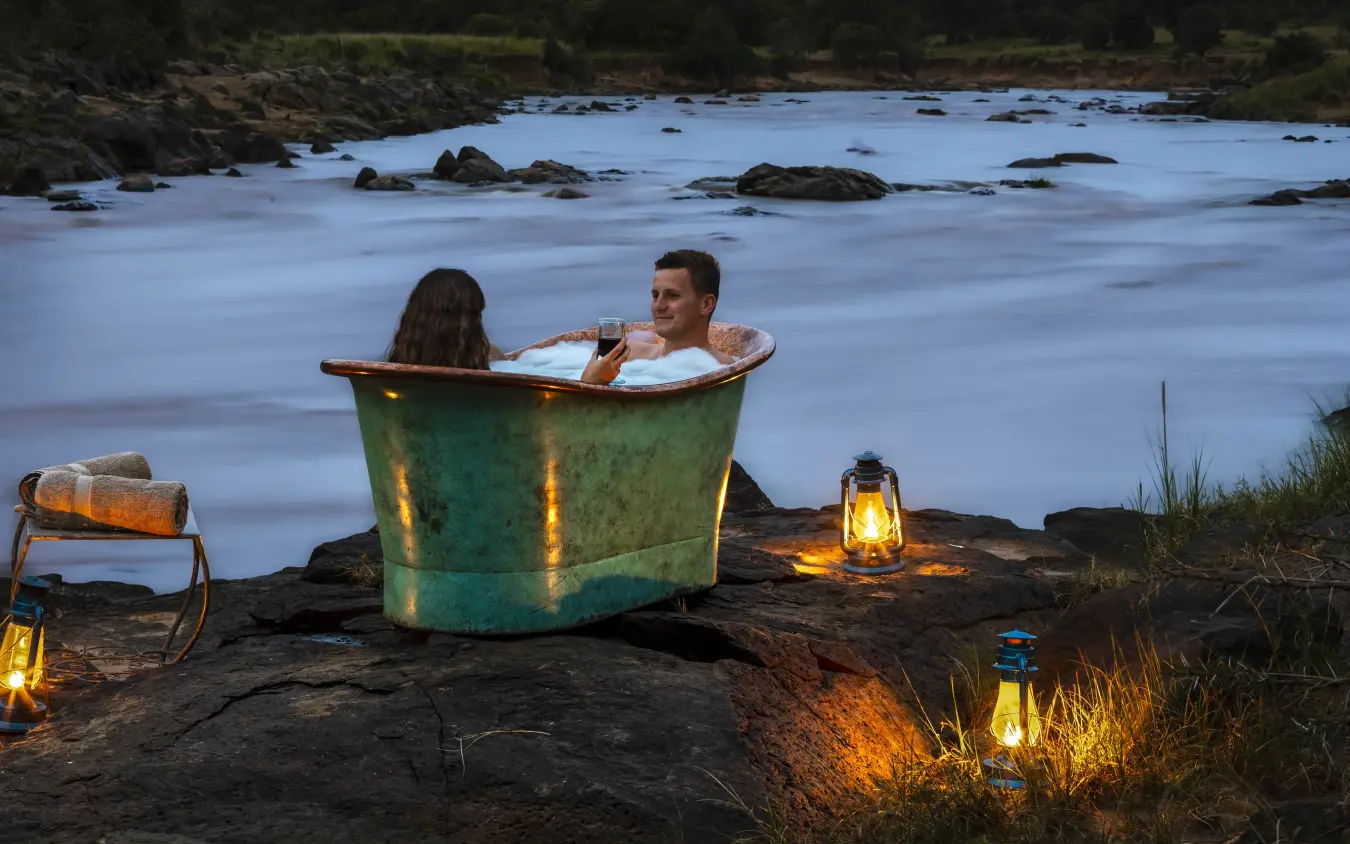 Couple bathing in vintage tub by river at dusk, Kimya Kimya Camp, Maasai Mara, Kenya