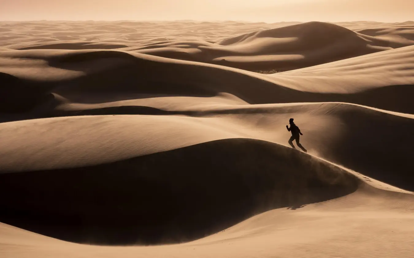 Solo traveler running across undulating sand dunes, Serra Cafema, Kunene River, Namibia