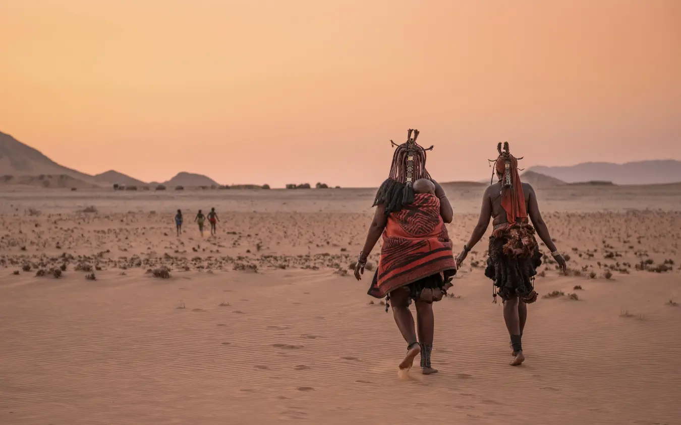 Two Maasai warriors walking across desert landscape at sunset, Serra Cafema, Kunene River, Namibia