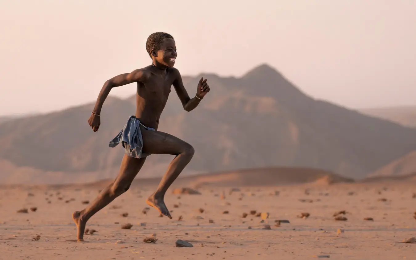 Child running across desert landscape with mountain backdrop, Kunene River, Namibia