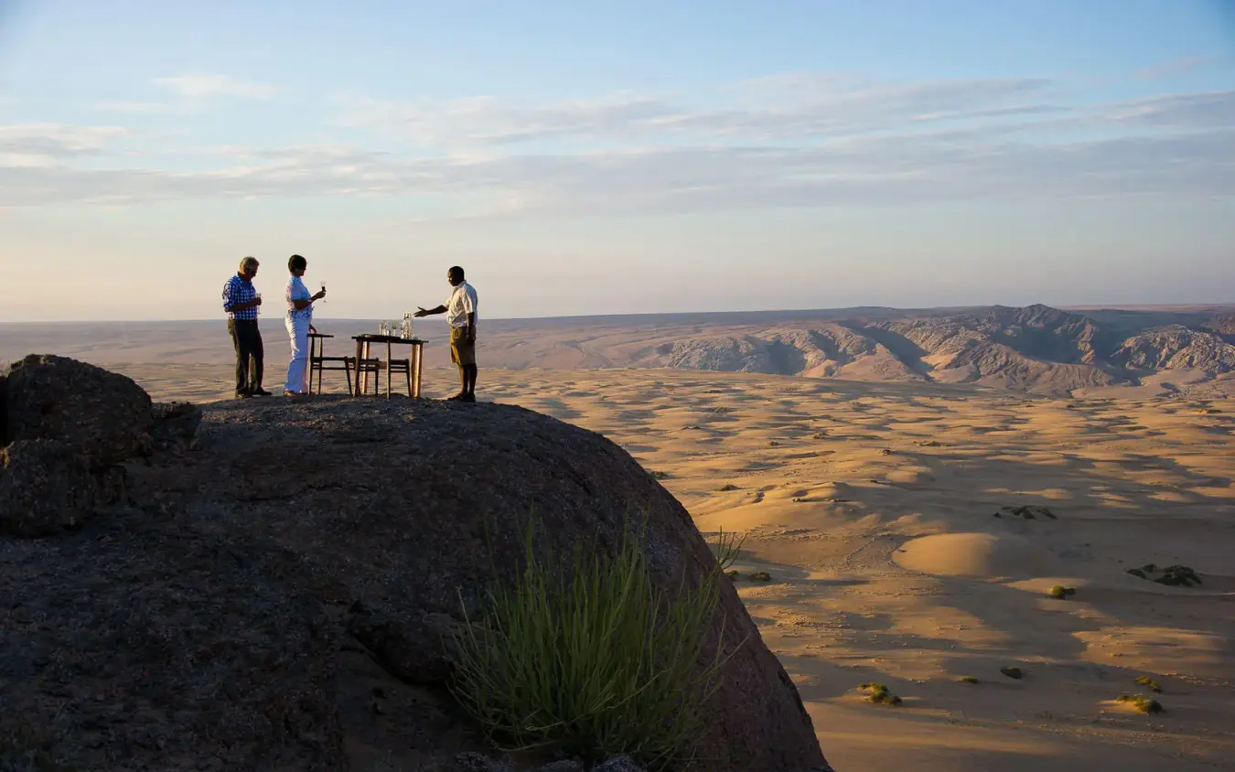 Guests dining on rocky outcrop overlooking vast desert landscape, Serra Cafema, Kunene River, Namibia