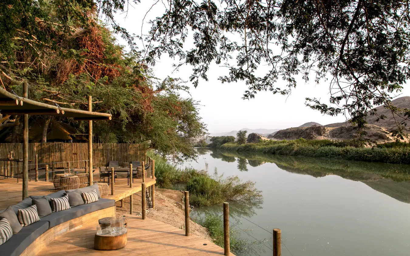 Wooden deck overlooking calm river with trees and mountains, Serra Cafema, Kunene River, Namibia