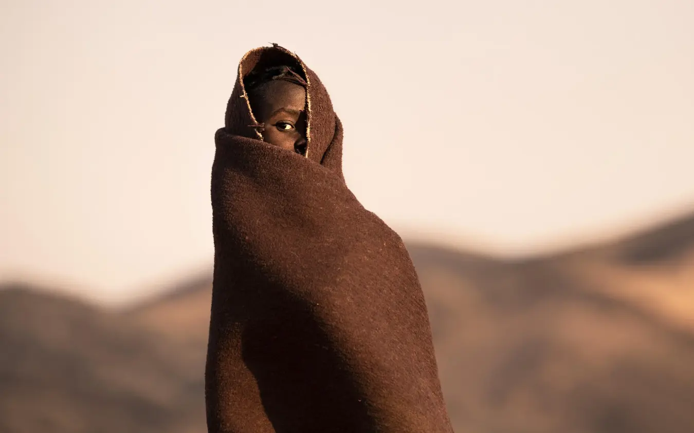 Person wrapped in brown blanket against desert landscape, Serra Cafema, Kunene River, Namibia