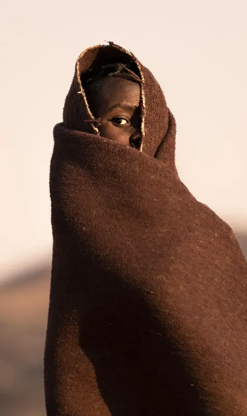 Person wrapped in brown blanket against desert landscape, Serra Cafema, Kunene River, Namibia