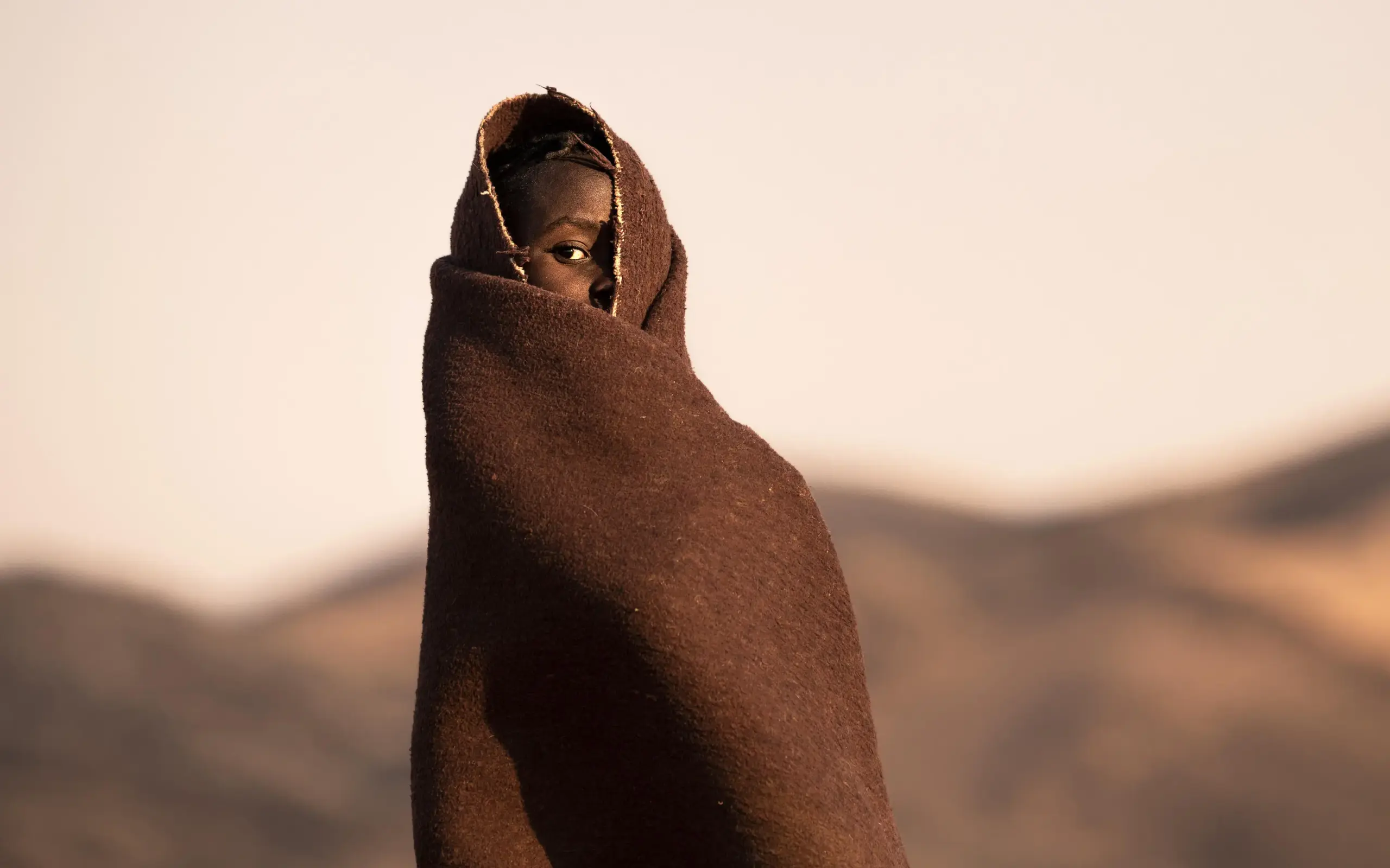 Person wrapped in brown blanket against desert landscape, Serra Cafema, Kunene River, Namibia