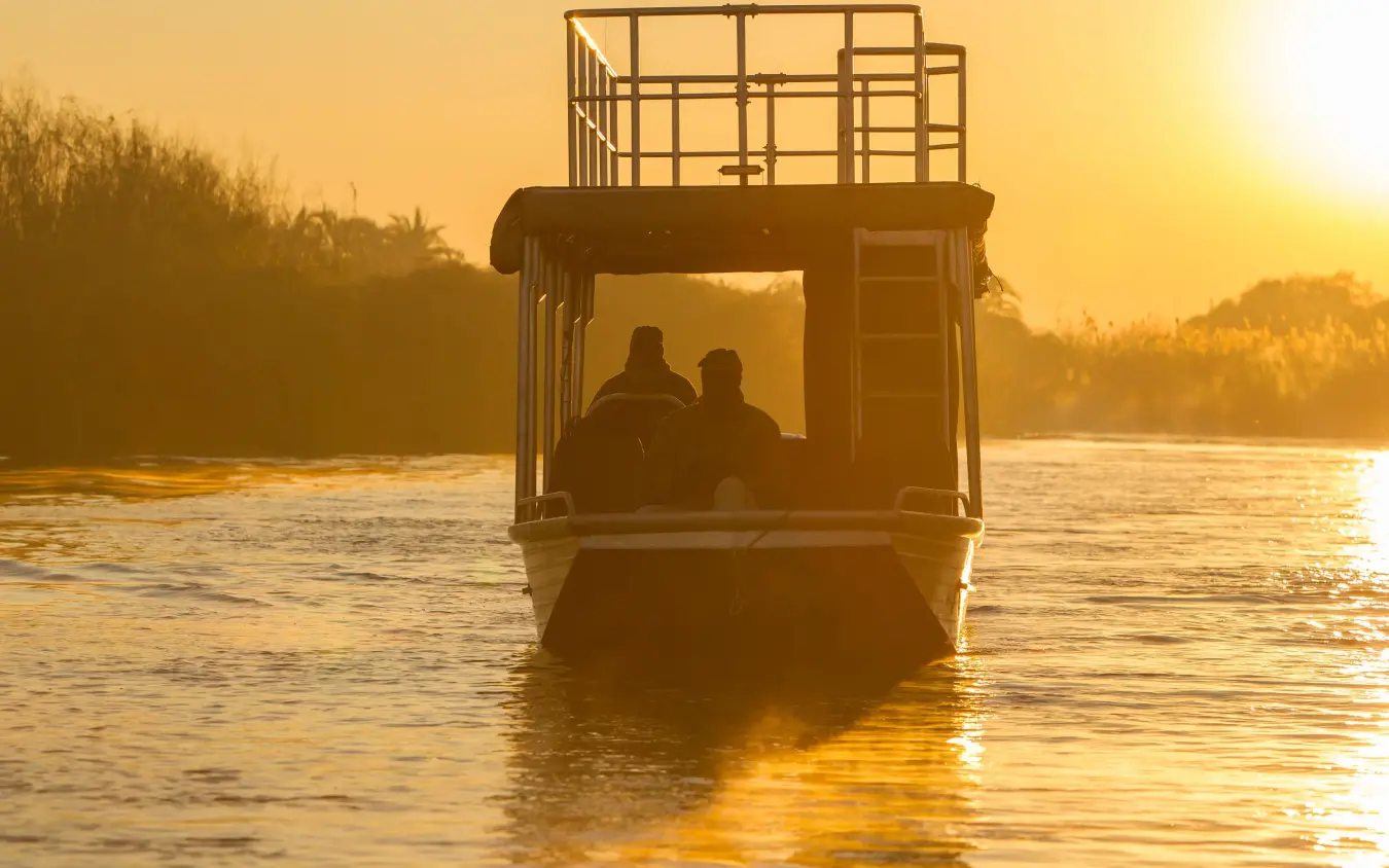Two people in boat cabin at golden sunrise on river, Setari, The Okavango Delta, Botswana