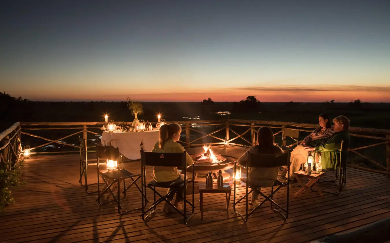 Guests gathered around fire pit on wooden deck at sunset, Setari, The Okavango Delta, Botswana