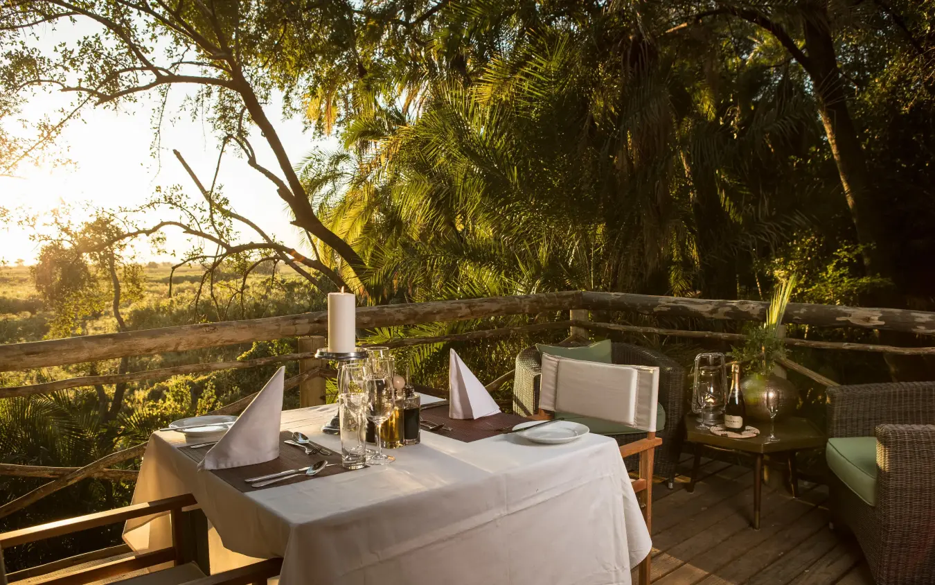 Dining table set on wooden deck overlooking savanna landscape, Setari, The Okavango Delta, Botswana
