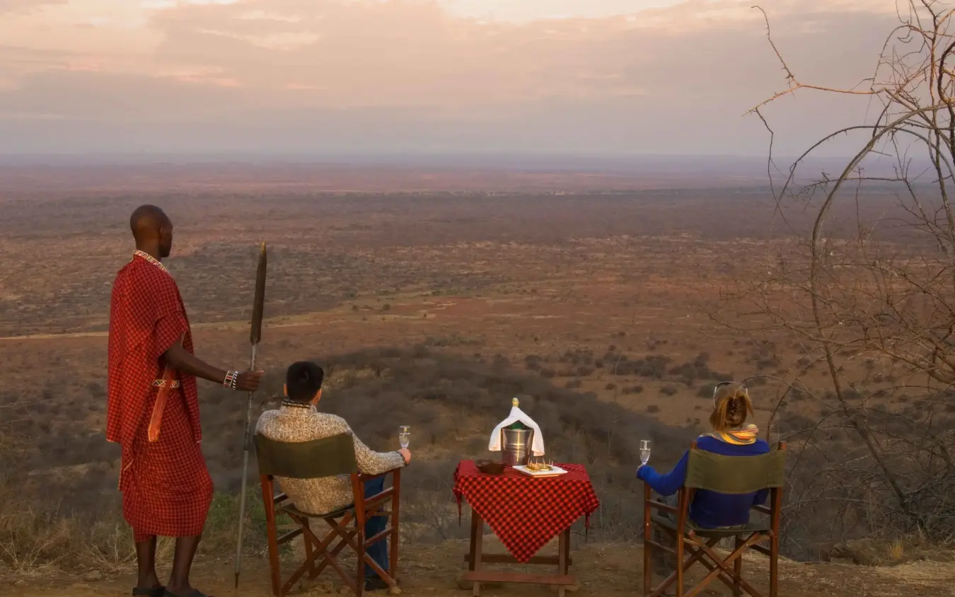 Guests dining at table overlooking vast savanna landscape at dusk, Severin Safari Camp, Tsavo, Kenya