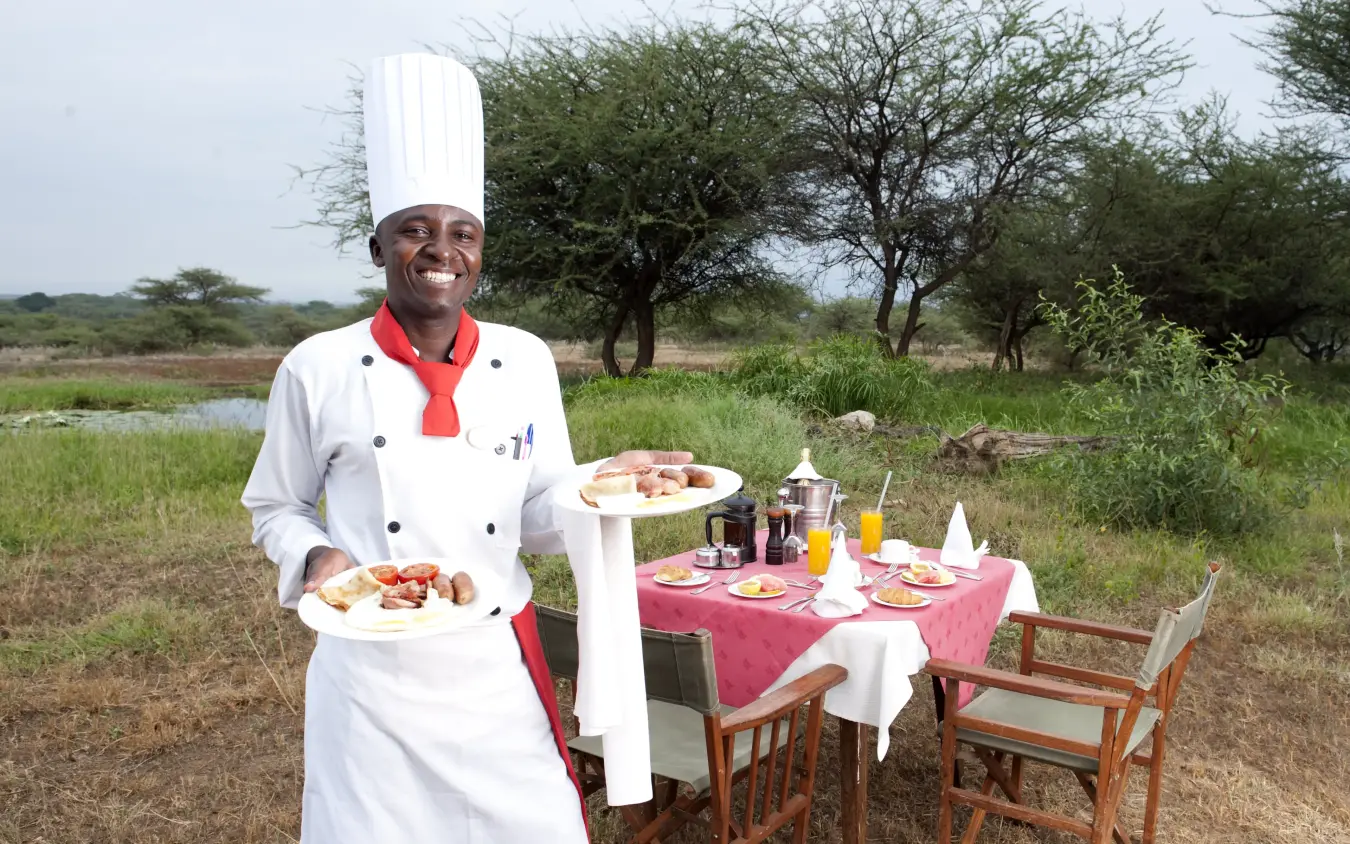 Chef presenting plated dishes at outdoor table in savanna landscape, Severin Safari Camp, Tsavo, Kenya