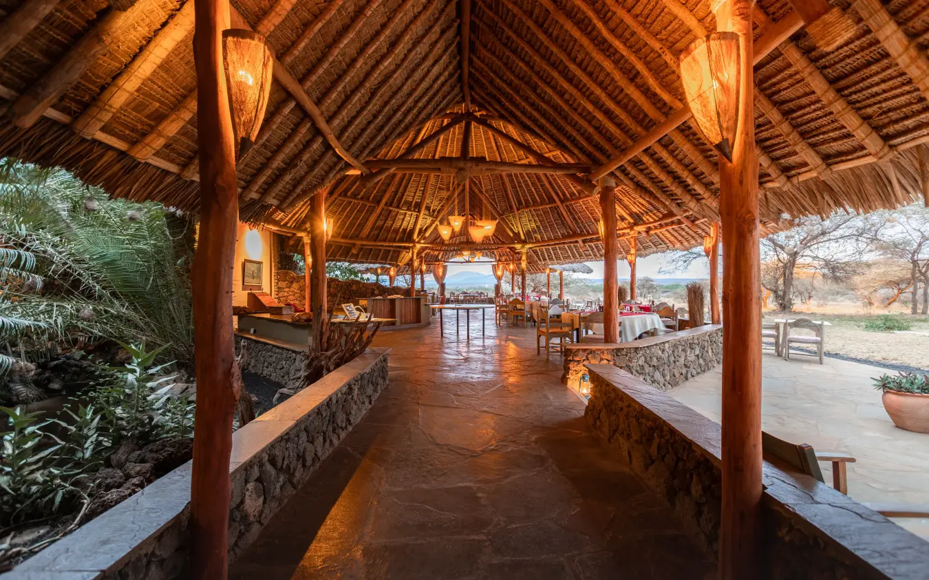Covered wooden pavilion with stone walls and lantern lighting at dusk, Severin Safari Camp, Tsavo, Kenya