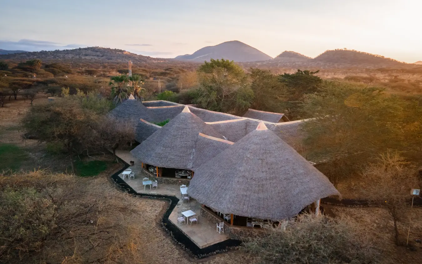 Thatched-roof lodge with multiple domes overlooking volcanic landscape at sunset, Severin Safari Camp, Tsavo, Kenya
