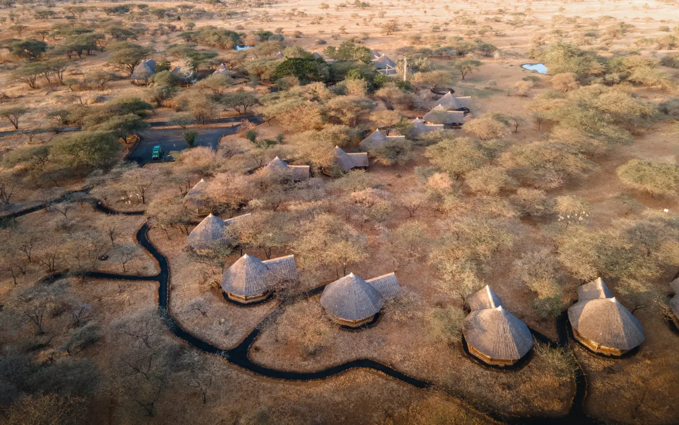 Aerial view of traditional thatched-roof lodge huts beside winding river in savanna, Severin Safari Camp, Tsavo, Kenya