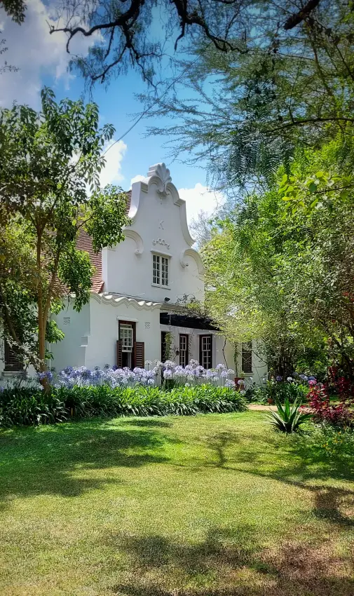 Historic whitewashed cottage surrounded by flowering gardens and mature trees