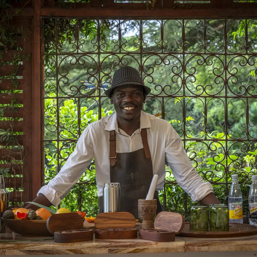 Bartender smiling behind wooden counter with ornate window, Sheba’s Secret Garden, Nairobi, Kenya