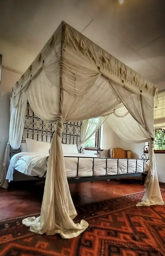 Four-poster bed with draped cream fabric canopy in bedroom with ornate headboard, Sheba’s Secret Garden, Nairobi, Kenya