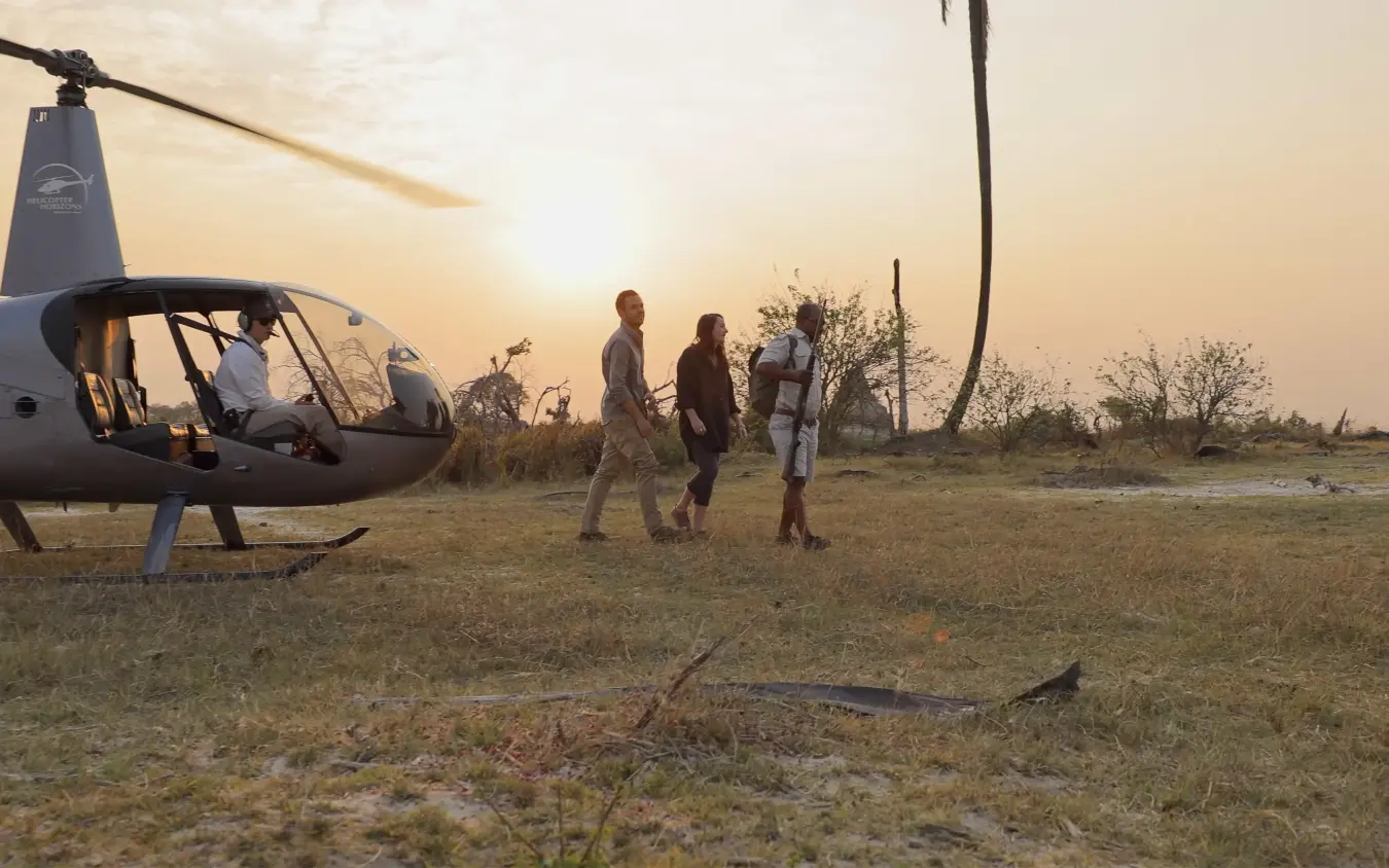 Guests boarding helicopter at sunset in savanna landscape, Shinde, The Okavango Delta, Botswana