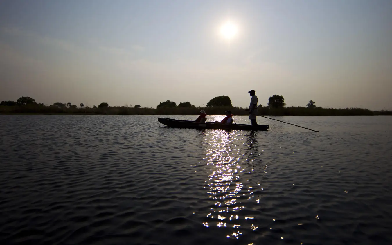 Boatman poling traditional boat at sunrise over water, Shinde, The Okavango Delta, Botswana