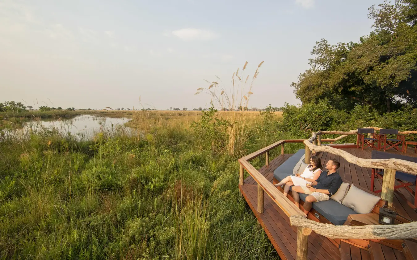 Guests relaxing on wooden deck overlooking wetland landscape, Shinde, The Okavango Delta, Botswana