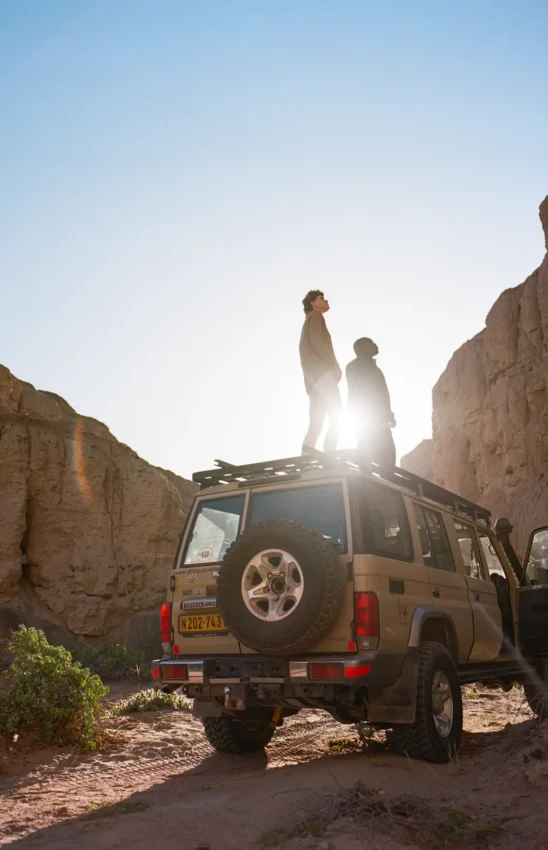 Guests standing on safari vehicle roof in desert canyon, Shipwreck Lodge, Skeleton Coast, Namibia