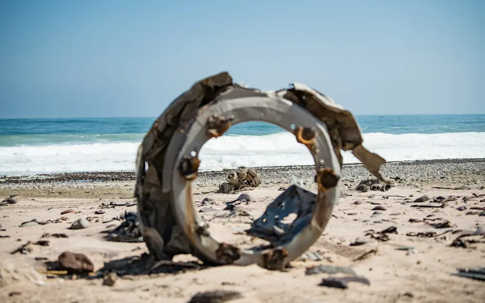 Rusted metal wheel on beach with ocean waves behind, Shipwreck Lodge, Skeleton Coast, Namibia
