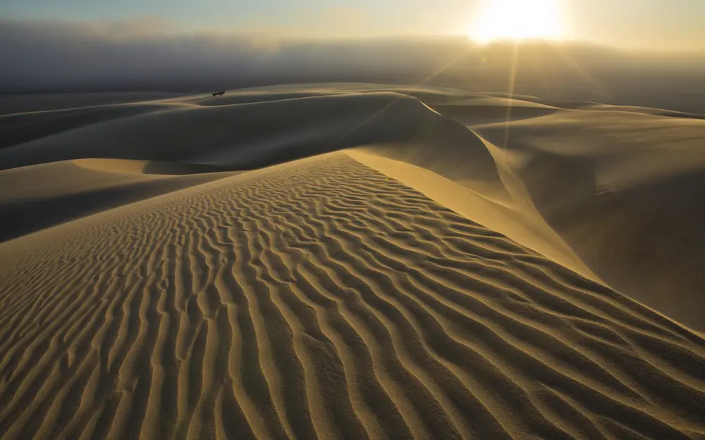 Sand dunes at sunrise with vehicle in distance, Shipwreck Lodge, Skeleton Coast, Namibia