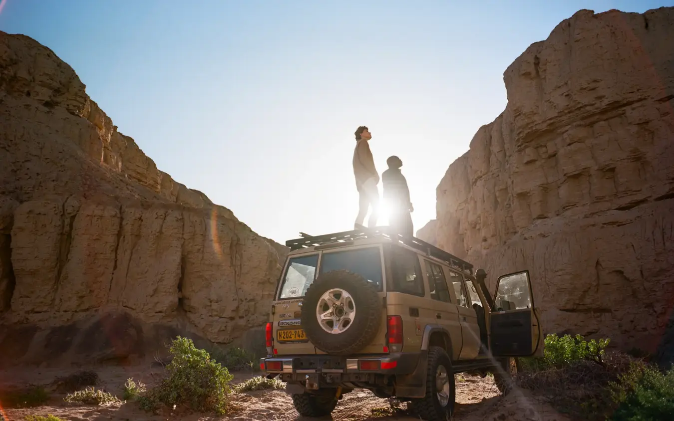 Guests standing on safari vehicle roof in desert canyon, Shipwreck Lodge, Skeleton Coast, Namibia