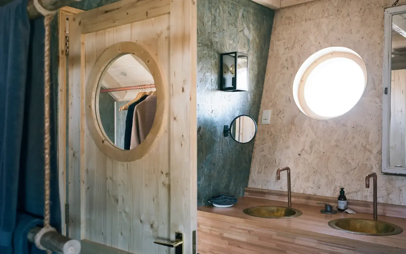 Bathroom with dual sinks, wooden mirror frame, and circular window, Shipwreck Lodge, Skeleton Coast, Namibia
