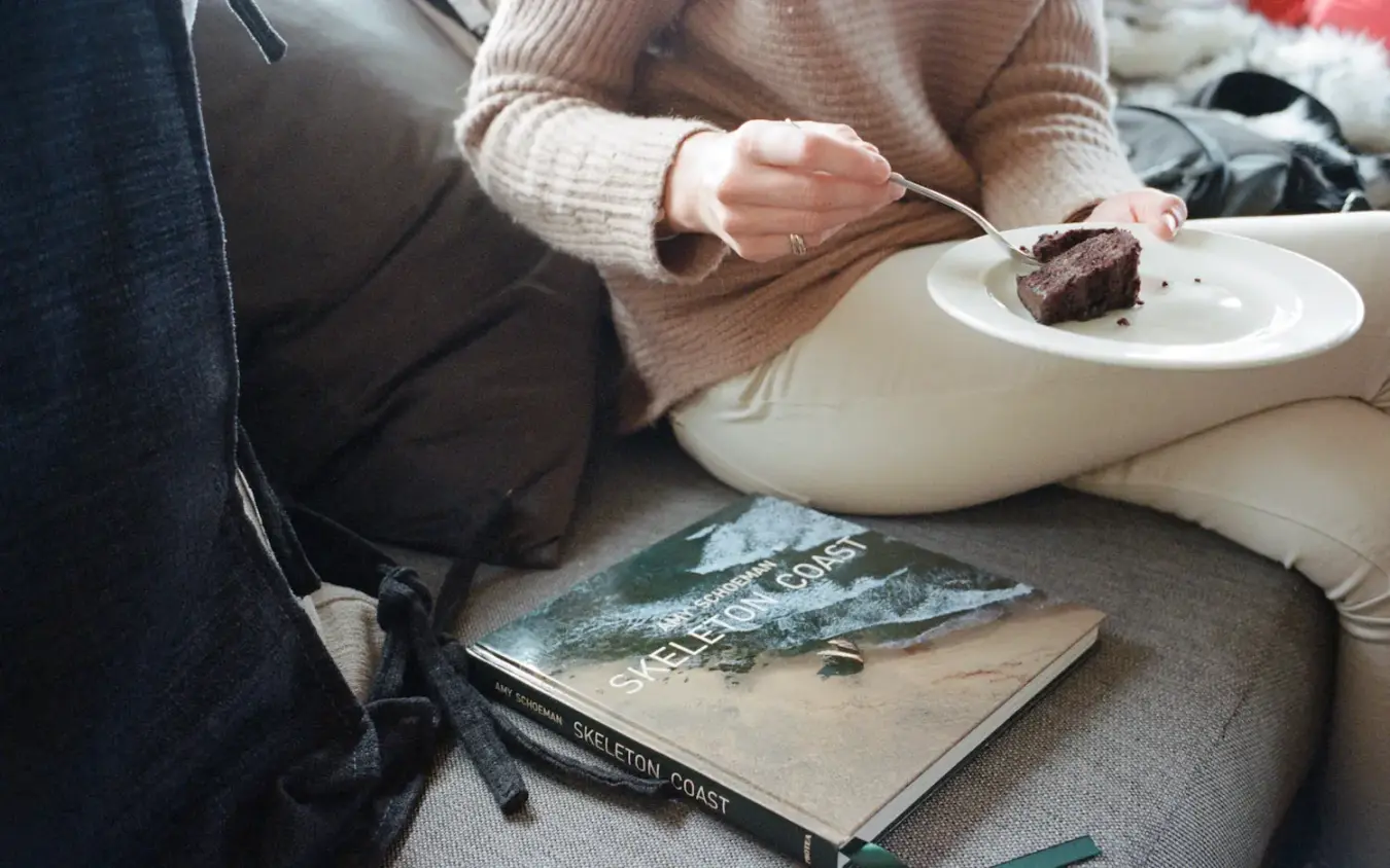 Guest enjoying chocolate cake with book while relaxing indoors, Shipwreck Lodge, Skeleton Coast, Namibia