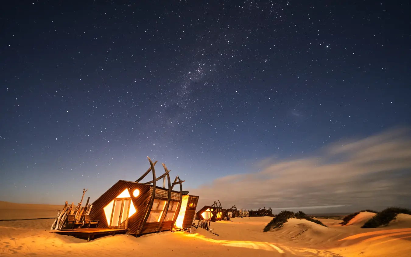 Illuminated lodge structure in desert at night under stars, Shipwreck Lodge, Skeleton Coast, Namibia
