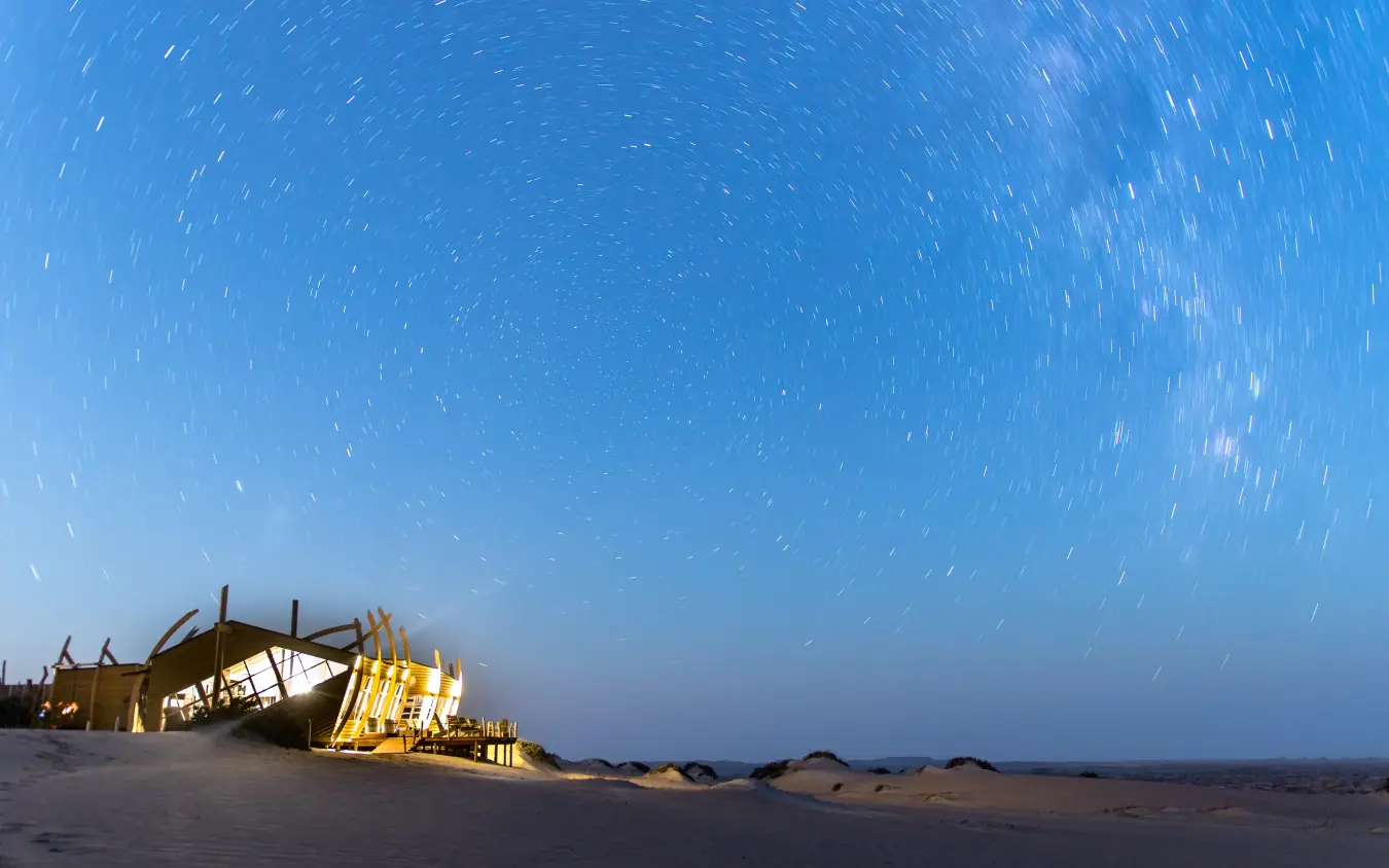 Illuminated lodge structure on desert sand at twilight, Shipwreck Lodge, Skeleton Coast, Namibia