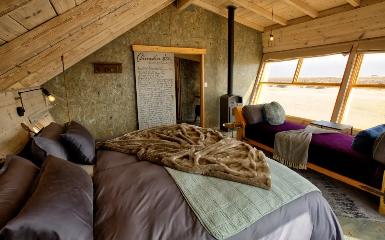 Bedroom interior with large windows overlooking desert landscape, Shipwreck Lodge, Skeleton Coast, Namibia