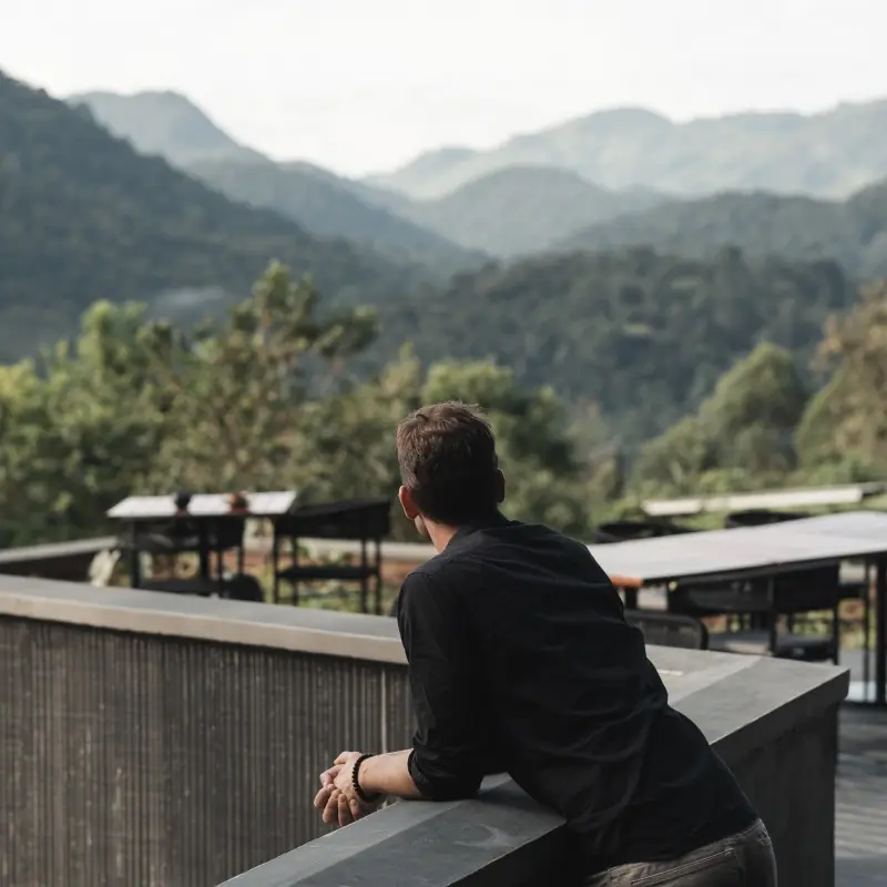 Man on deck overlooking forested mountain valley with modern architecture, Silverback Lodge, Bwindi Impenetrable Forest, Uganda