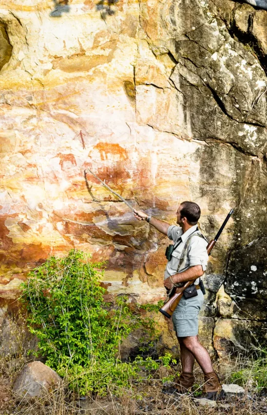 Hunter examining ancient rock art on cave wall, Singita Malilangwe House, Gonarezhou & Malilangwe, Zimbabwe