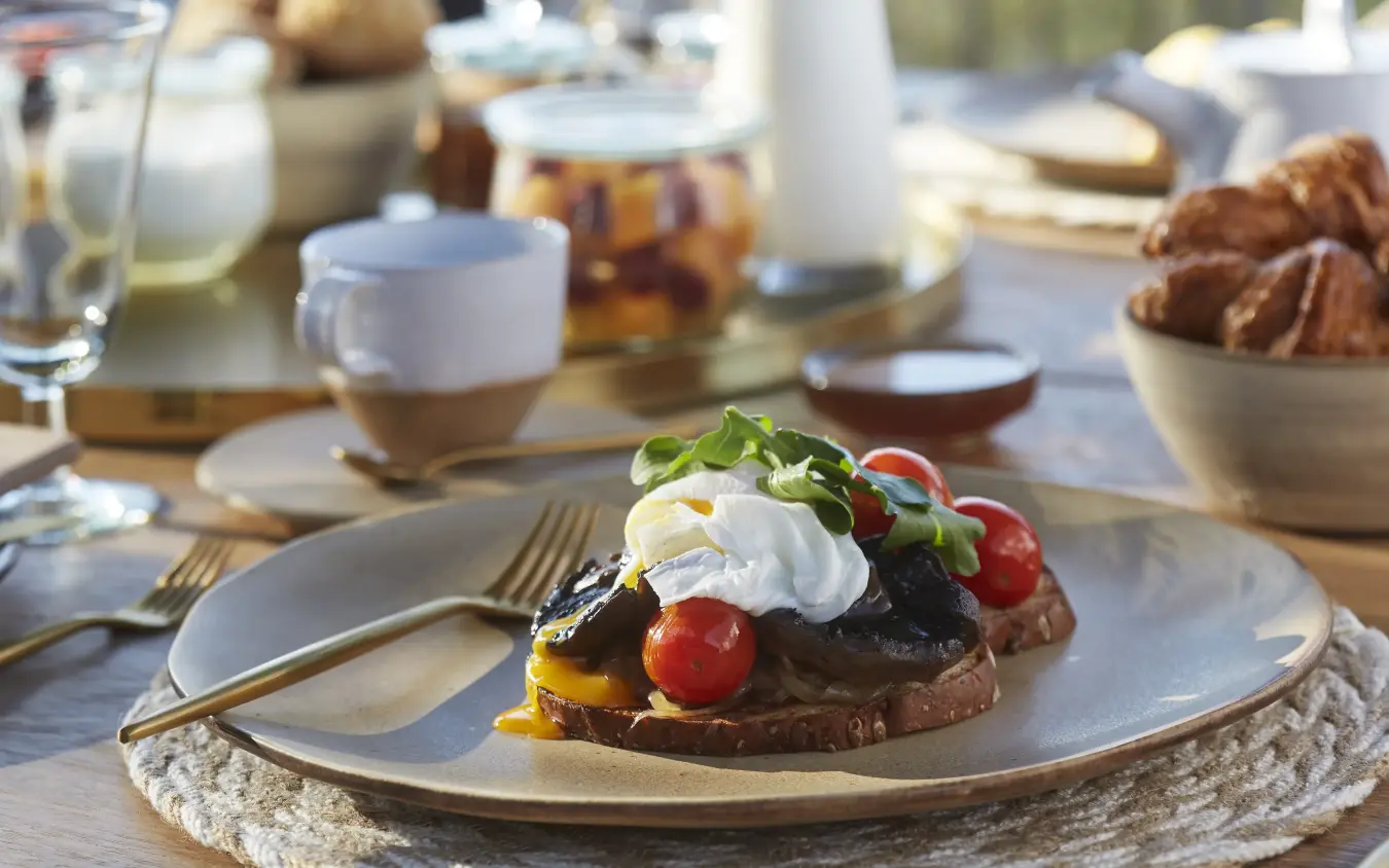 Outdoor breakfast table with poached egg toast and fresh berries in sunlight, Singita Malilangwe House, Gonarezhou & Malilangwe, Zimbabwe
