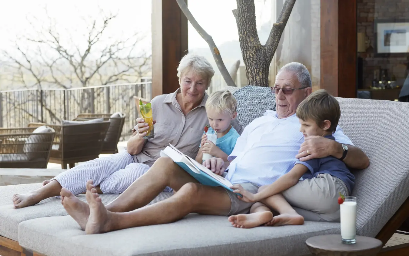 Grandparents and grandchildren relaxing on outdoor sofa with savanna view, Singita Malilangwe House, Gonarezhou & Malilangwe, Zimbabwe