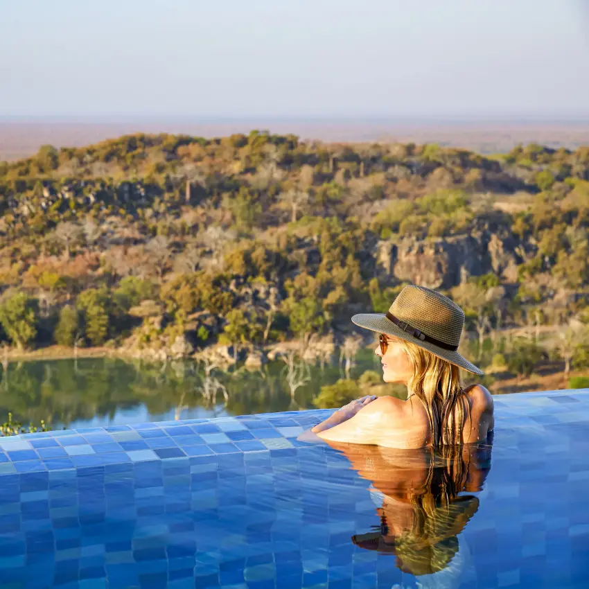 Woman in infinity pool overlooking river and forested valley, Singita Malilangwe House, Gonarezhou & Malilangwe, Zimbabwe