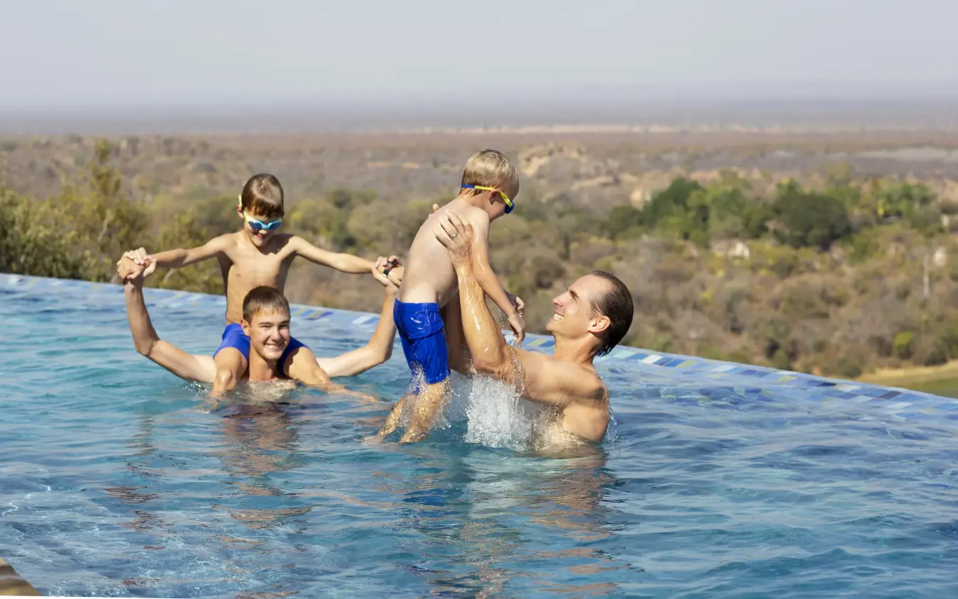 Family swimming in infinity pool overlooking savanna landscape, Singita Malilangwe House, Gonarezhou & Malilangwe, Zimbabwe