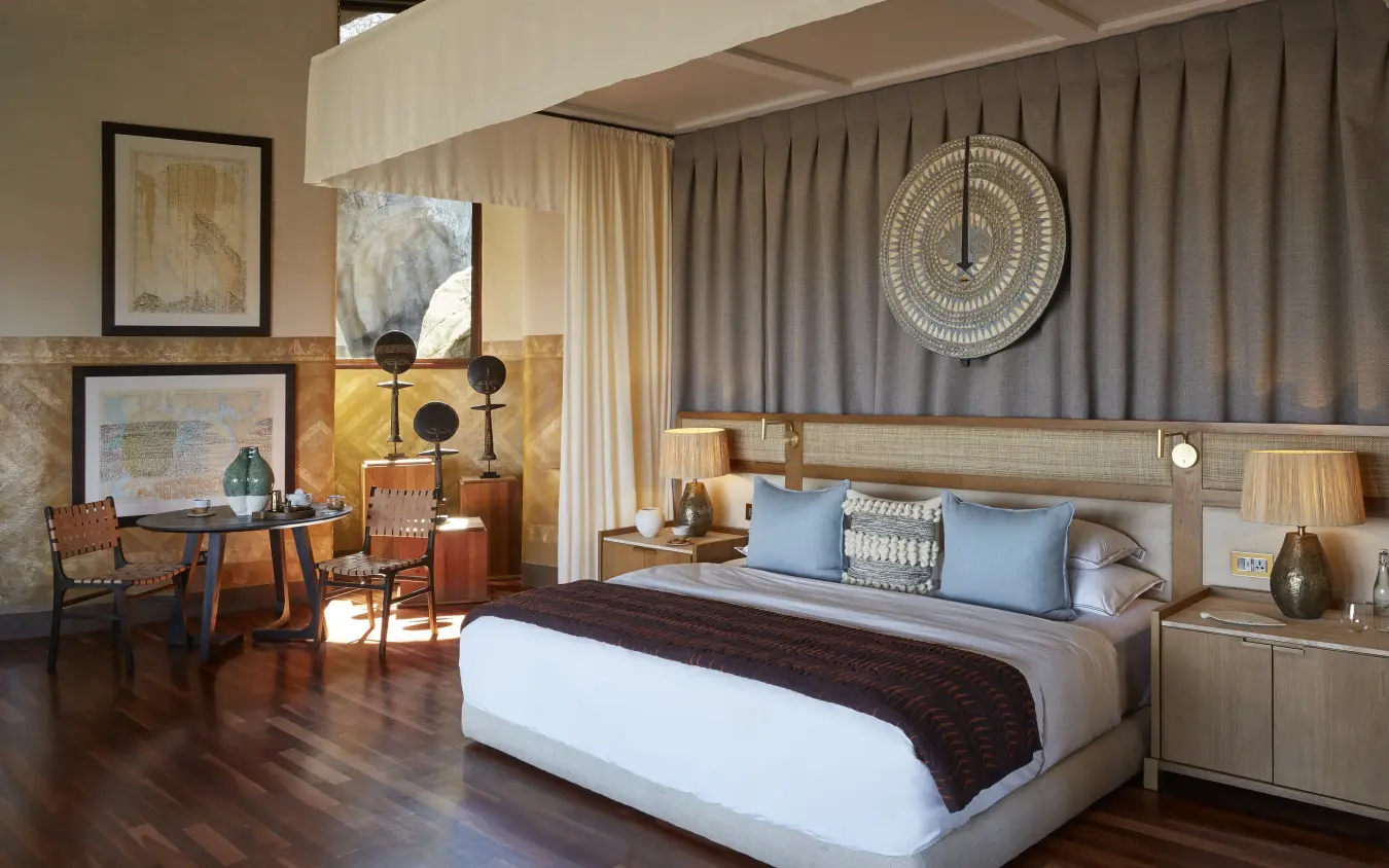 Modern hotel bedroom with wooden furnishings and decorative tribal wall art, Singita Malilangwe House, Gonarezhou & Malilangwe, Zimbabwe