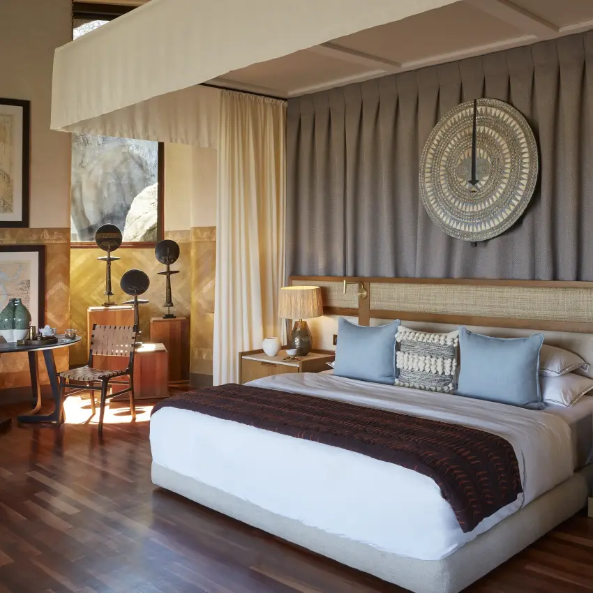 Modern hotel bedroom with wooden furnishings and decorative tribal wall art, Singita Malilangwe House, Gonarezhou & Malilangwe, Zimbabwe