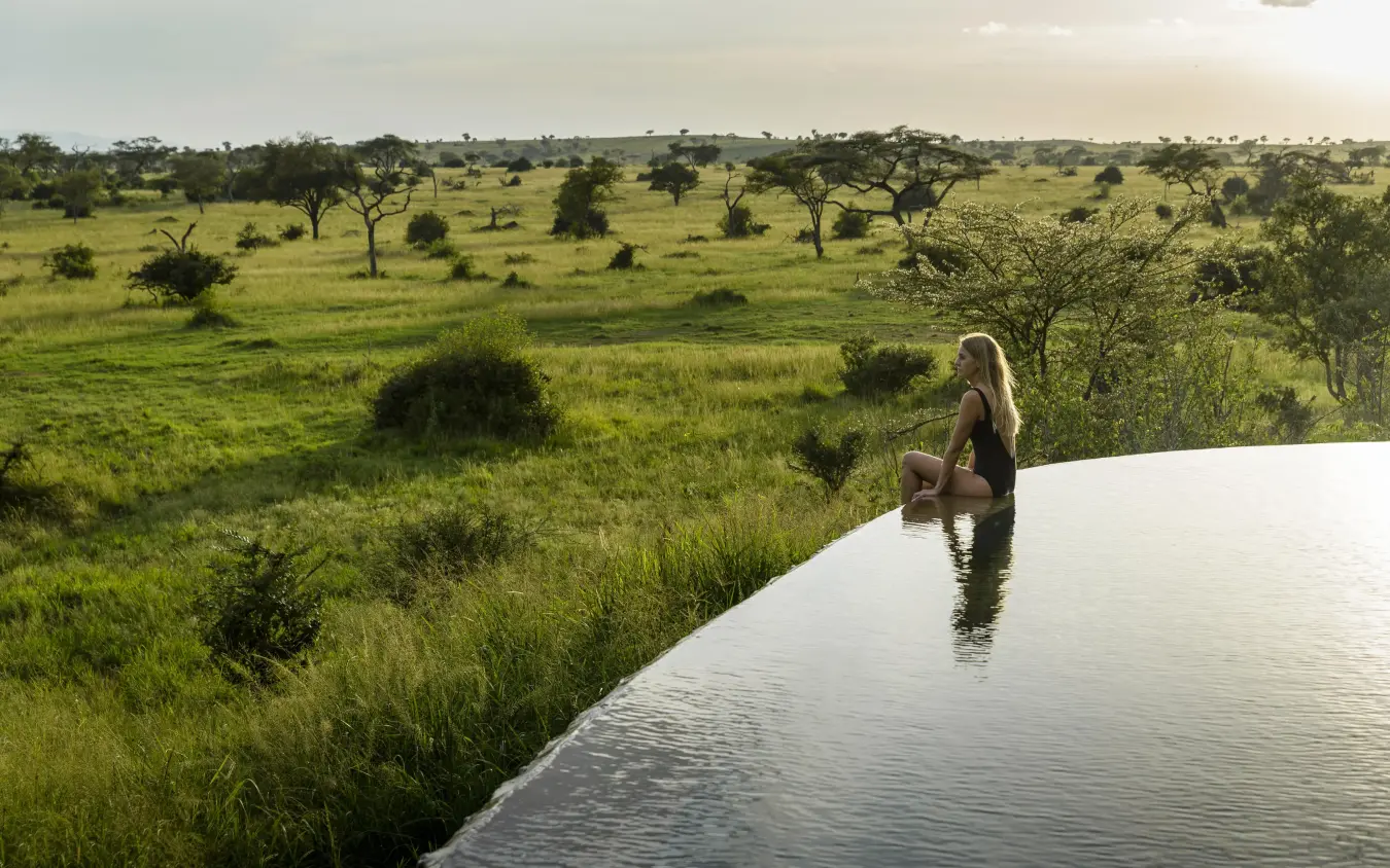 Woman sitting at edge of infinity pool overlooking savanna, Singita Sasakwa Lodge, Serengeti National Park, Tanzania