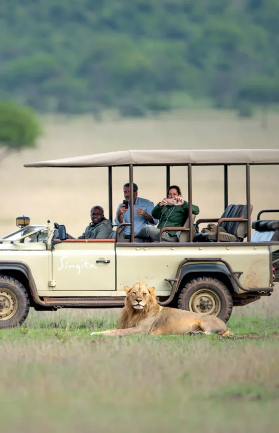 Safari vehicle with guests observing lion in grassland, Singita Sasakwa Lodge, Serengeti National Park, Tanzania