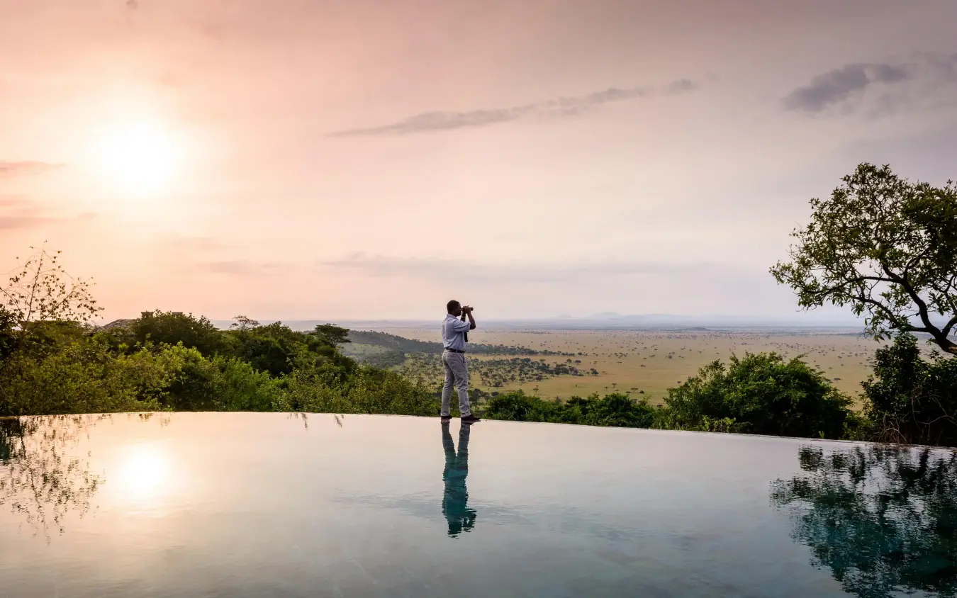 Person standing at infinity pool overlooking savanna at sunset, Singita Sasakwa Lodge, Serengeti National Park, Tanzania